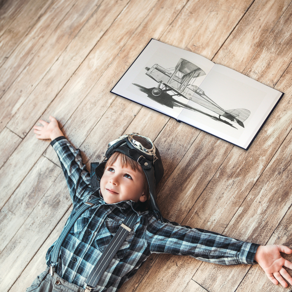 A child lying on a wooden floor with an open book showing a black and white illustration of a nautilus shell.
